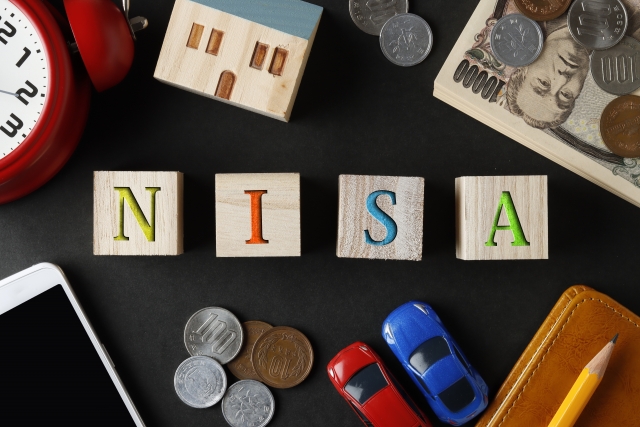 NISAと書かれたブロックとお金と文房具と時計と家や車の模型